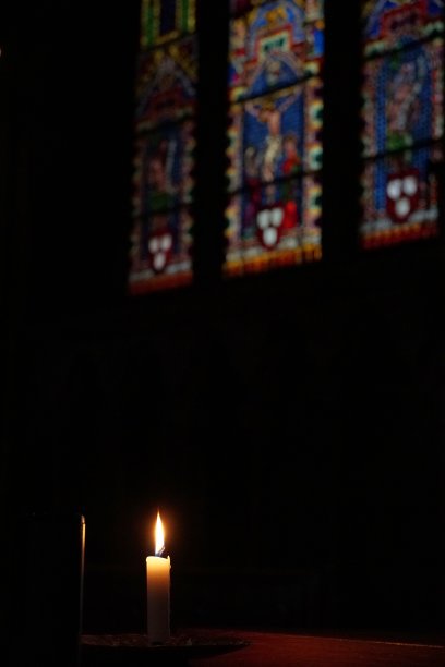 孤独的蜡烛在教堂黑暗的内部吹着。背景是一面深色的墙壁和装饰性的窗玻璃。有很大的复制空间。图片下载