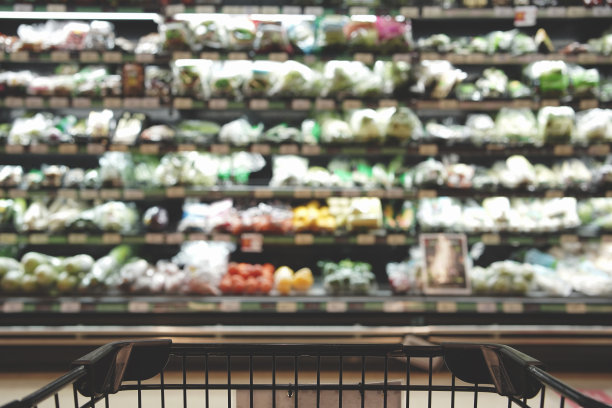 抽象模糊的超市货架与空的购物车在百货公司的照片。水果和蔬菜在货架上模糊的内部背景图片下载