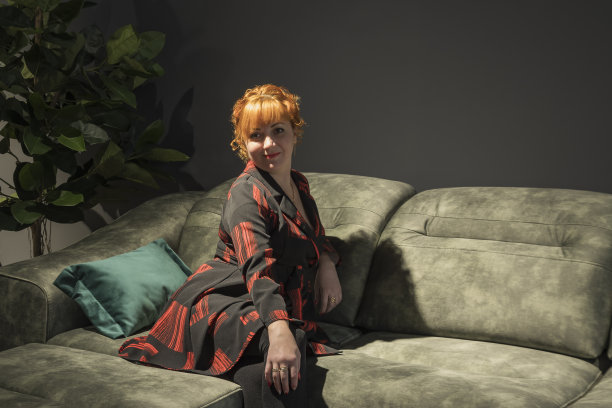 一个红头发的年轻女孩坐在黑房间的沙发上图片下载