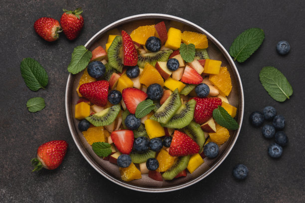 水果沙拉在碗棕色的背景。芒果、猕猴桃、橘子、苹果、草莓和蓝莓图片下载