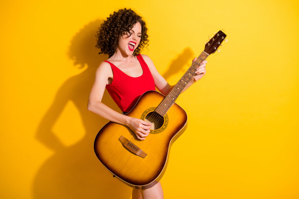 肖像照片的funky女孩与卷曲的头发大声唱歌，保持演奏音乐上的原声吉他在聚会孤立在生动的黄色背景图片下载