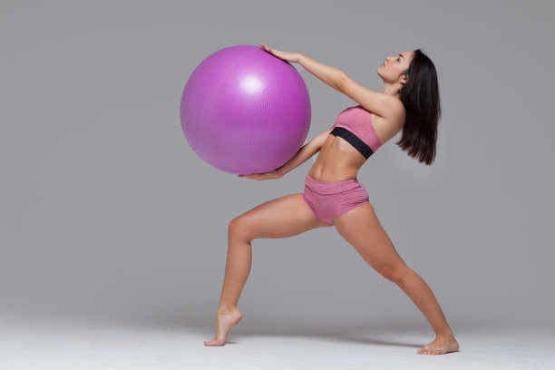 全长肖像的运动女孩在粉红色运动服摆姿势与健身球上方她的头孤立在灰色背景图片下载