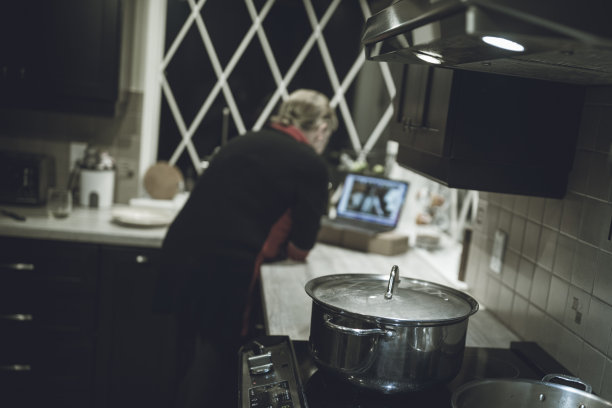 一位年长的女士把笔记本电脑放在厨房的柜台上，和一个网络小组一起，正在上一门烹饪课程，学习如何制作一种受欢迎的西非菜肴Yassa鸡肉。图片下载