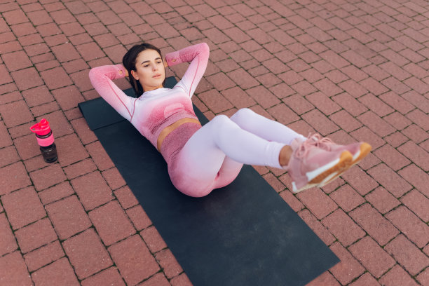 美丽的健身女人在粉红色运动服躺在瑜伽垫上，做腹部紧缩运动图片下载