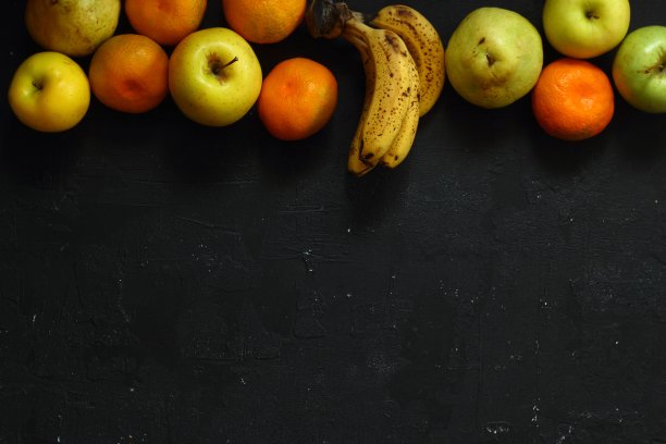 黑色背景上有许多成熟多汁的水果。苹果，梨，香蕉和桔子一起吃。图片下载