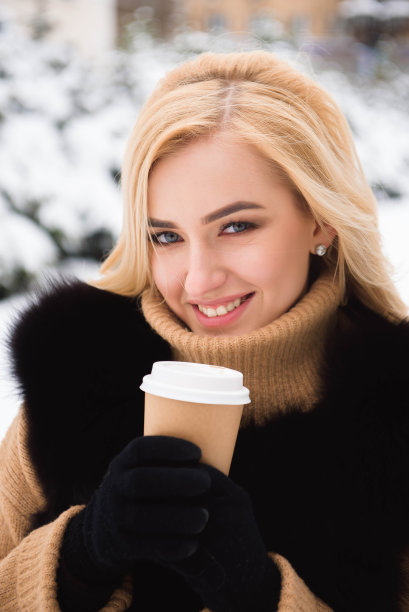 欧洲时尚女性在冬季公园喝咖啡的肖像。图片下载