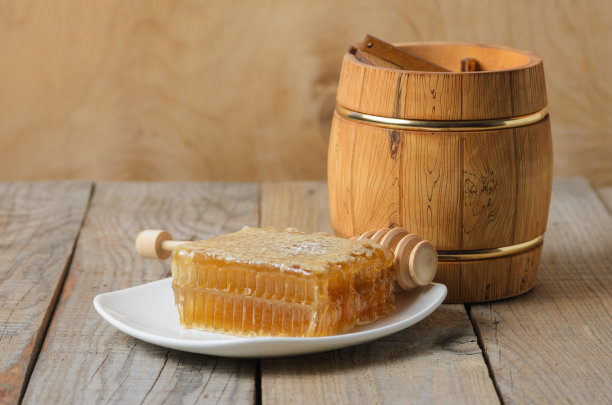 蜂蜜蜂窝状装在白色盘子上，木质罐子和勺子放在粗糙的木质背景上。图片下载
