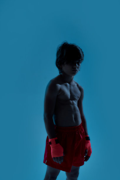 这是一个穿着短裤、手上缠着拳击绷带的小男孩的剪影，他站在蓝色背景下孤立地看着镜头图片下载