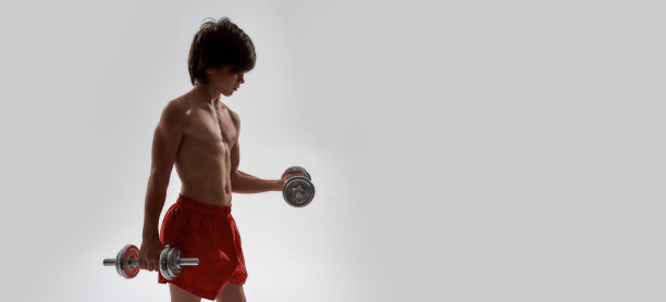 运动的小男孩与肌肉的身体锻炼，显示他的肌肉，举重，而孤立地站在灰色的背景图片下载