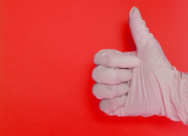 一只戴着白色乳胶手套的手在红色背景上竖起大拇指图片下载
