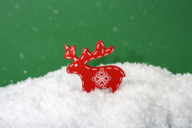 木制圣诞鹿雕像在雪上的绿色背景与雪花图片下载