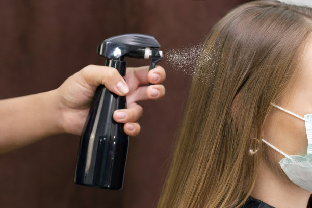 由于冠状病毒大流行，年轻女子戴着防护口罩在美发店工作图片下载