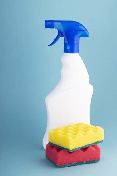 白色塑料喷瓶里的窗户清洁剂和蓝白色背景上的彩色海绵图片下载