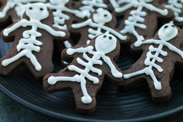 特写图片的黑色盘子自制，人的形状，巧克力饼干，饼干冰为骷髅与白色糖霜，重点前景，万圣节主题的派对食品图片下载