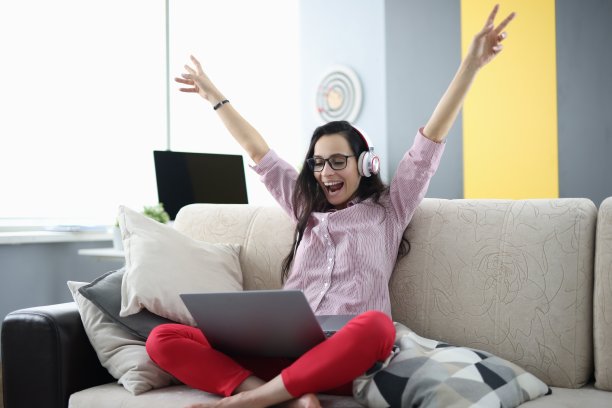 戴着耳机的女人坐在房间的沙发上，满心欢喜。图片下载