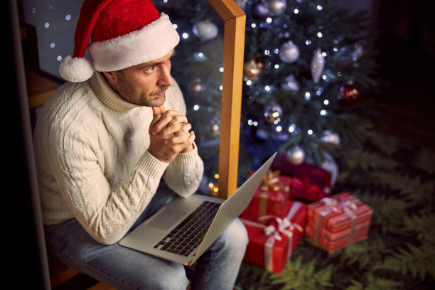 乐观的英俊男子想与膝上型电脑在圣诞树附近的家图片下载