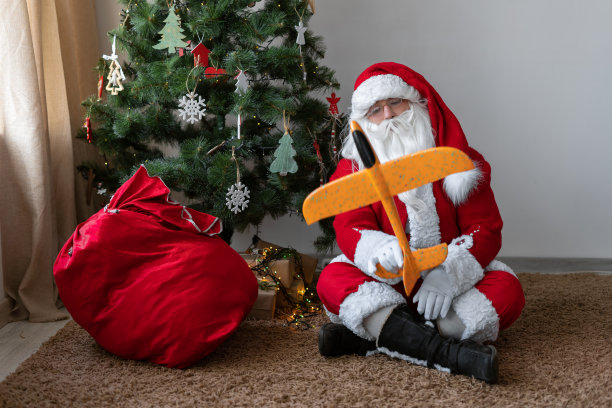 圣诞老人累了。圣诞老人坐在地板上，拿着一袋礼物，玩着玩具飞机。假期过后他累了。图片下载