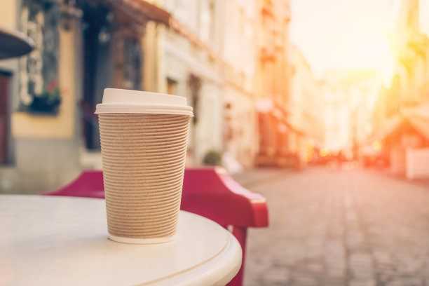 纸杯咖啡外卖的模型图像，站在木桌上模糊的咖啡馆后面作为背景与复制空间。咖啡装在可回收的纸杯里图片下载
