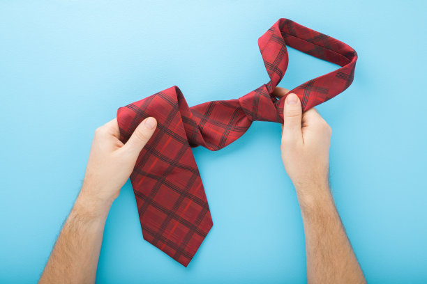 年轻的成年男子手握深红色的领带在浅蓝色的桌子背景。柔和的颜色。特写镜头。视角拍摄。自顶向下的观点。图片下载