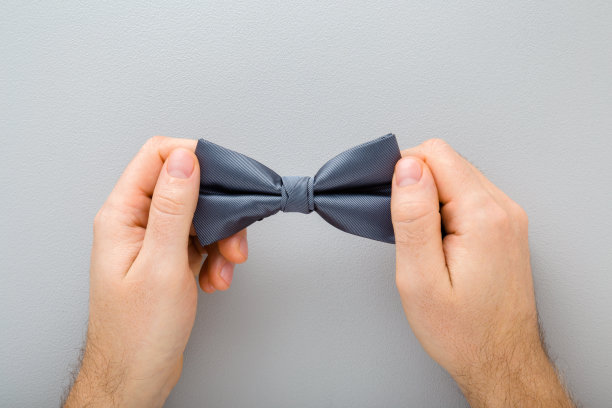 年轻的成年男子手握深色领结在浅灰色的桌子背景。特写镜头。视角拍摄。自顶向下的观点。图片下载
