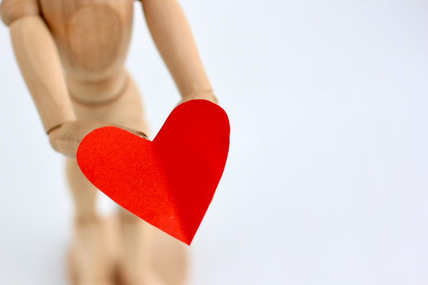 灰色背景下，木制模特手里拿着红纸做的心。时尚简约的情人节概念，爱，真实的感觉。副本的空间。图片下载