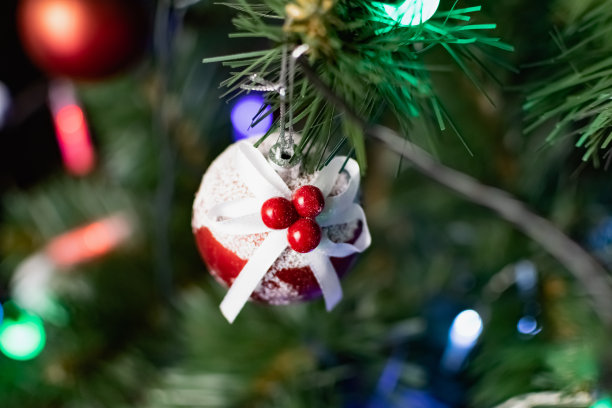人造圣诞树的树枝上挂着鲜红色的圣诞玩具。雪球和浆果。各种各样的节日饰品在彩色花环旁闪闪发光图片下载