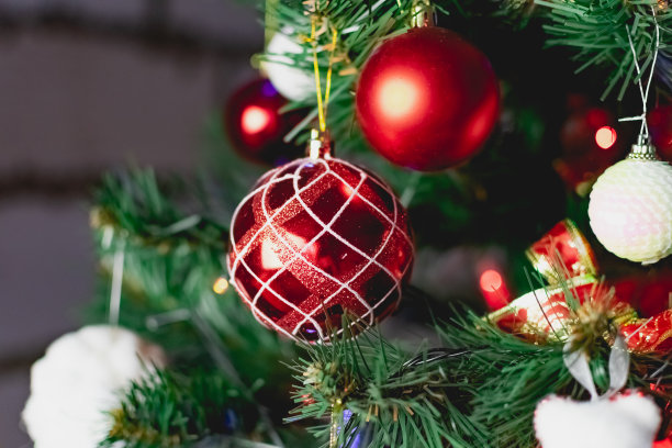 人造圣诞树的树枝上挂着鲜红色的圣诞玩具。雪球和浆果。各种各样的节日饰品在彩色花环旁闪闪发光图片下载
