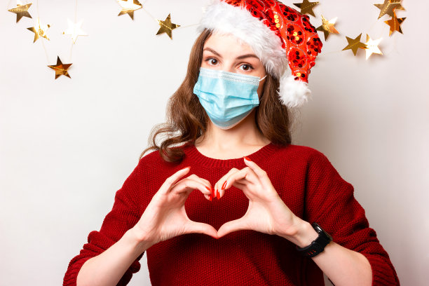 年轻女孩穿着红色毛衣，戴着医用口罩，象征着新年和圣诞节的爱和心图片下载