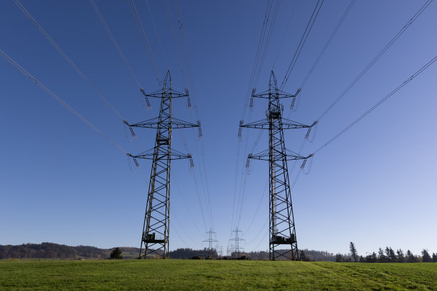 两根巨大的高压电线杆在秋日碧蓝的天空上，在绿色的草地上，可以看到更多的电线杆在背景中，电力在我们的现代社会是至关重要的图片下载
