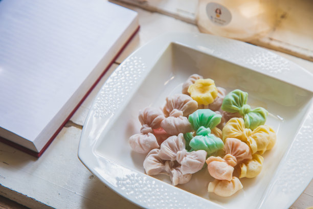 诱惑泰国糖果在白色的圆盘上，在白色的木桌和一本打开的书。图片下载