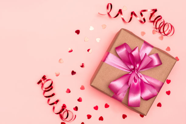 带有粉色丝带的礼盒和心形纸屑，并在粉红色的背景下装饰彩带。图片下载