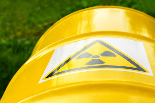 靠近绿色草地上黄色金属桶上的核标志。辐射危险标志。放射性废物图片下载