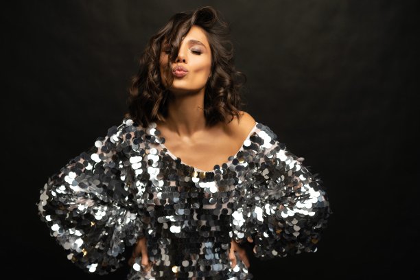 美丽性感的女人穿着在黑色的背景上闪闪发光的裙子。图片下载
