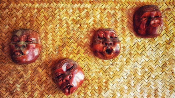 四个民族木纹面具点缀在竹墙背景上图片下载