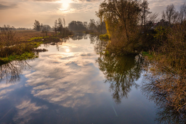 一条河中树和云的倒影的背光照片。美丽的日落天空在背景。图片来自瑞典斯卡尼亚县图片下载