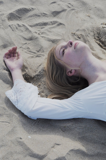 年轻美丽的女孩躺在沙滩上的沙滩上图片下载