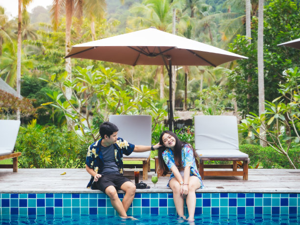 年轻的亚洲夫妇在度假胜地的游泳池旁享受暑假旅行。图片下载