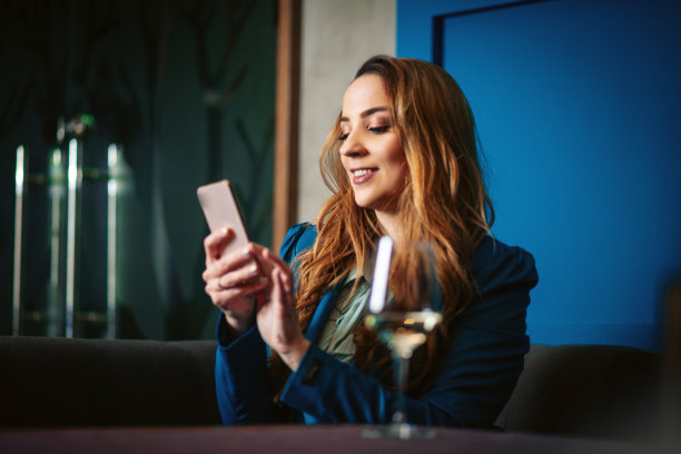 微笑的女人喝白葡萄酒和使用电话在餐厅图片下载