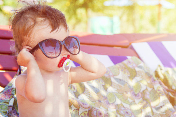 可爱的孩子戴着墨镜坐在热带沙滩上的躺椅上图片下载