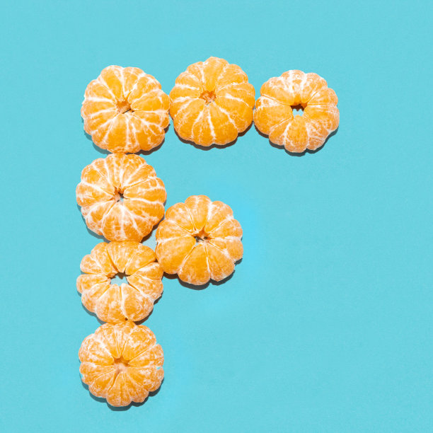 在蓝色背景下，用剥了皮的橘子拼出字母F。Flatlay。图片下载