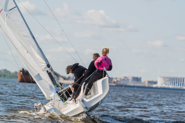 一幅美丽的图片，背景是一艘运动游艇在一条宽阔的河流上满帆漂浮的城市景观图片下载