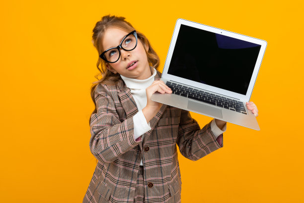 惊喜美丽的女孩在一个经典的夹克显示笔记本电脑与模型显示向前黄色背景与复制空间图片下载