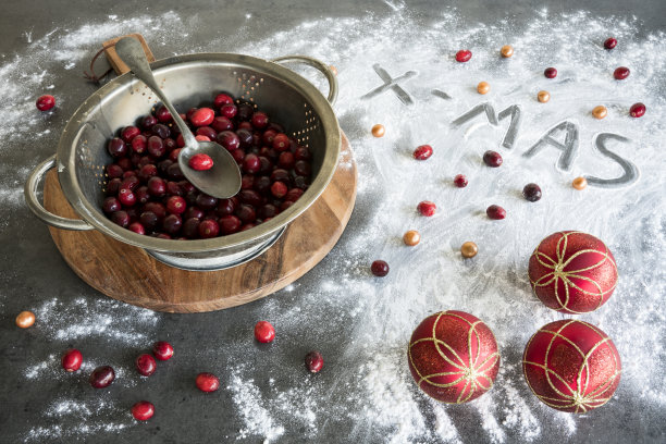 鲜红的蔓越莓装在金属滤锅里，还有圣诞球和文字。图片下载