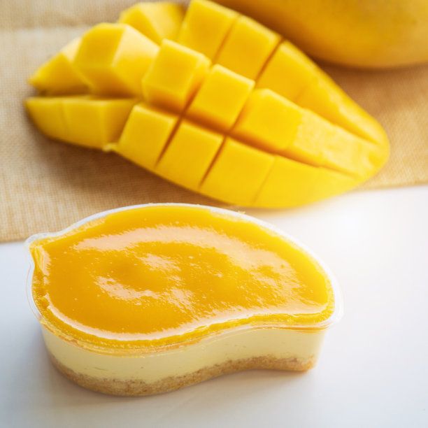 在白色的盘子上切成薄片的芒果薄饼，上面点缀着芒果和薄荷，放在一张白色的桌子上，以芒果和绿色的自然为背景。图片下载