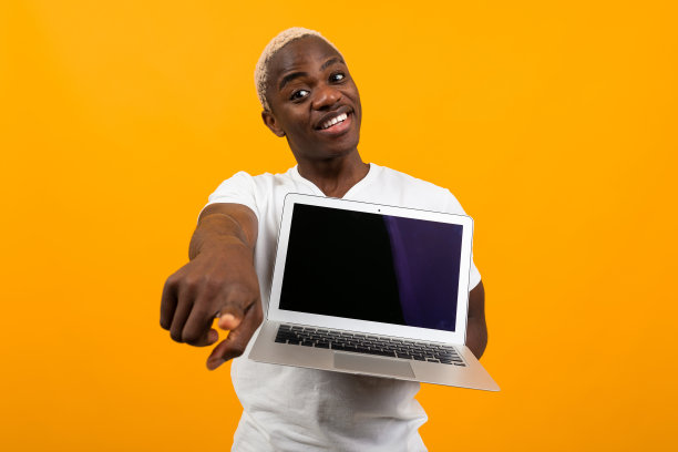 微笑可爱的美国人在白色t恤显示笔记本电脑显示模型和指向向前的手指在橙色工作室背景图片下载