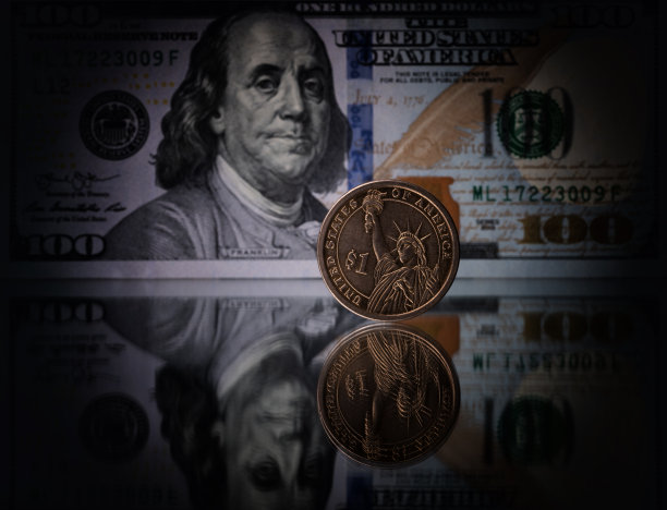 一枚1美元硬币在一张100美元纸币的背景上立在镜面上图片下载