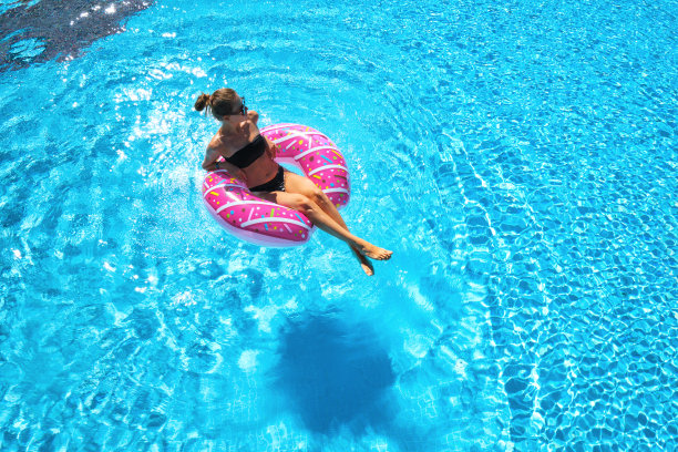 美丽的年轻女子游泳在粉红色的甜甜圈游泳环透明的蓝色水在夏季日落。热带山水与性感苗条的女孩在池中，清澈的水。前视图。旅行。鸟瞰图图片下载
