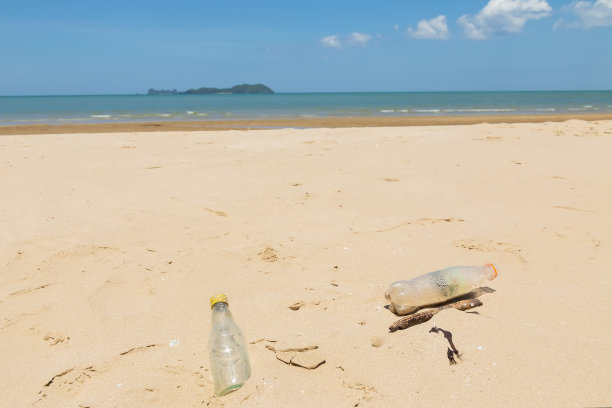 海滩上的垃圾和蓝天。白天海滩上的玻璃和塑料瓶。海洋污染的概念。图片下载