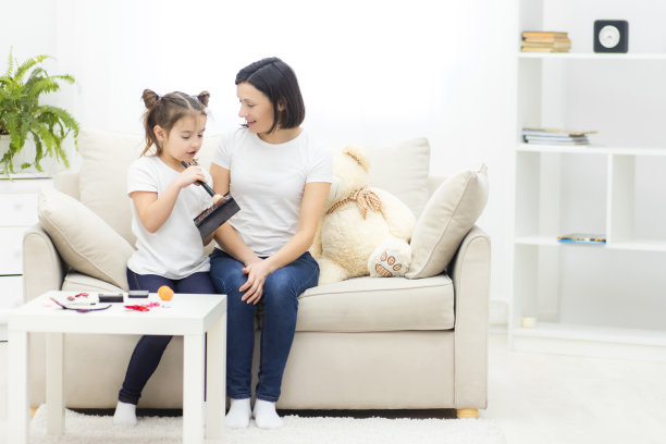 一张小女孩在沙发上为妈妈化妆的照片。图片下载