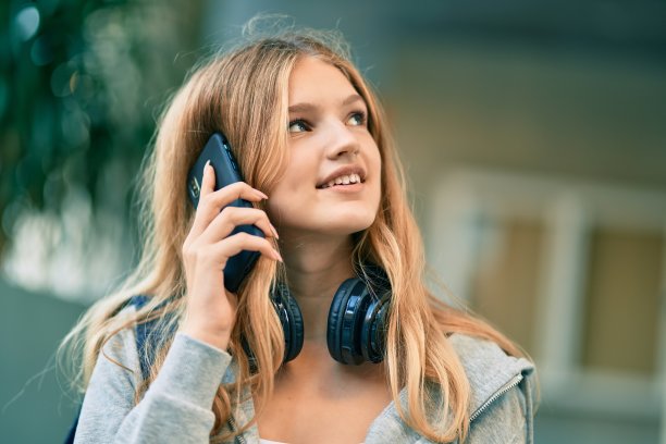 美丽的白人学生少年在大学愉快地谈论智能手机。素材图片